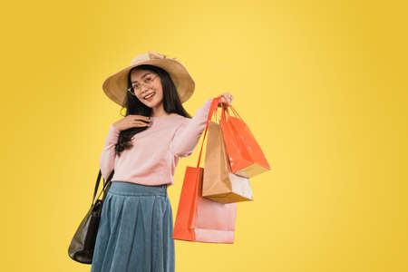 Beautiful woman in hat and glasses smiling with hand carrying shopping paper bagの写真素材