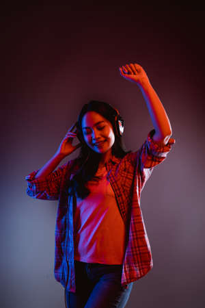 woman dancing while listening to music with headphones in dark roomの写真素材