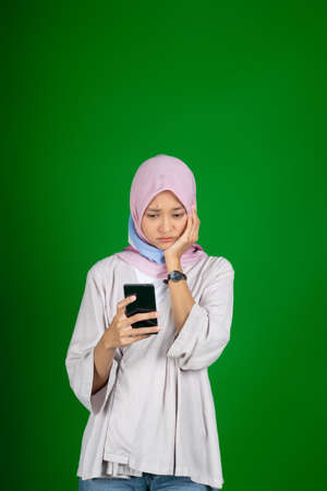 asian girl in hijab sad when looking at phone screenの写真素材
