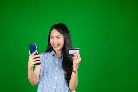 Excited asian woman while using a mobile phone hold credit cardの写真素材