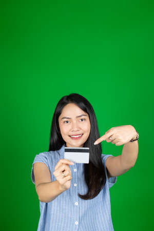asian woman looking at camera while holding atm card with hand gesture pointingの写真素材
