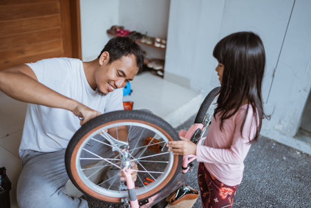 Asian father using wrench to repair bicycle with daughter