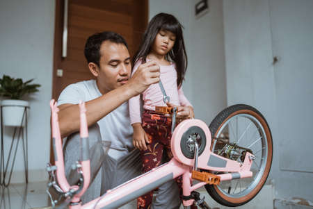 Father attaching a bicycle pedal with his daughterの写真素材