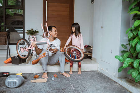 Father holding bicycle frame and daughter carrying wheelsの写真素材
