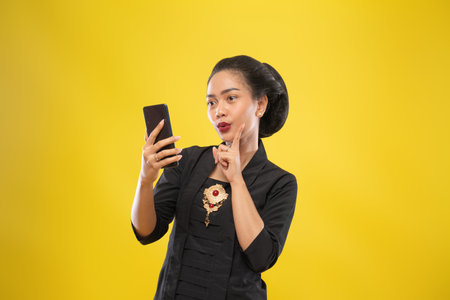 Javanese woman with traditional Kebaya dress thinking gesture holding smartphone