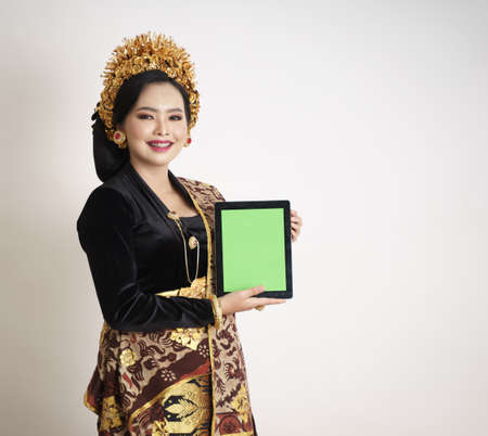 Smiling balinese woman wearing traditional clothes showing digital tabletの写真素材