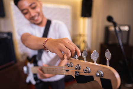 selective focus of a male bassists hand tuning an electric guitar bass string before playingの写真素材