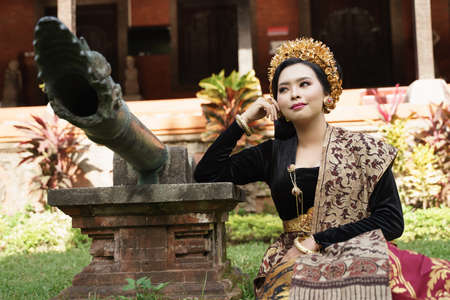woman wearing Balinese kebaya sitting next to the statueの写真素材