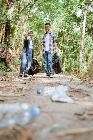 two happy teenage volunteers picking up trashの写真素材