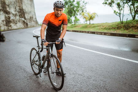 male cyclist pushing his bike and walk after struggling to climbの写真素材