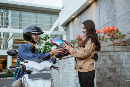 Asian woman receiving helmet from man riding motorbike on roadsideの写真素材