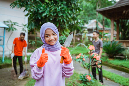 Smiling girl wearing gloves with thumbs up holding earthen shovelの写真素材