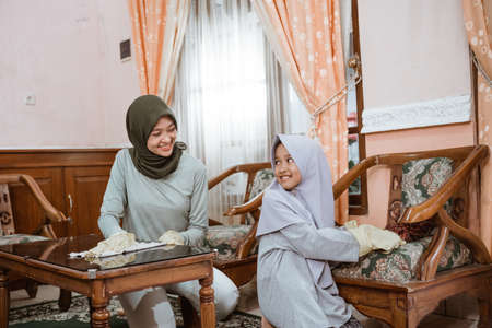Mother in veil and daughter chatting while cleaning the houseの写真素材