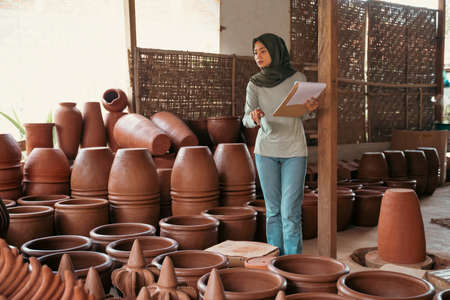 veiled businesswoman counting pottery holding clipboard at ceramic pottery stallの写真素材
