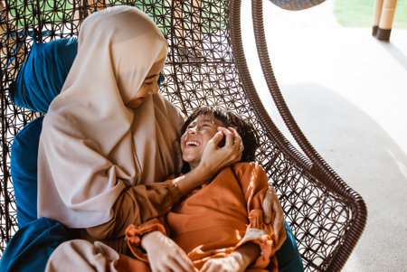 muslim mother and daughter sitting and cuddling on a chair togetherの写真素材