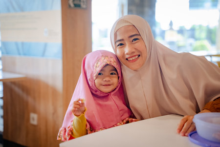 muslim young girl while sitting on dining room with mother smiling to cameraの写真素材