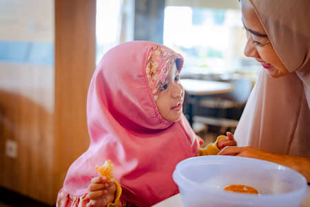 mother and daughter eating pancake. muslim asian family having breakfastの写真素材