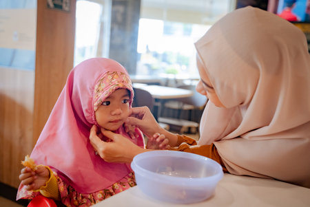 mother fixing her daughters hijab while having breakfastの写真素材