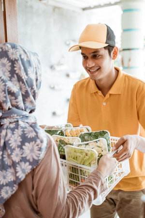 Deliveryman gives vegetable orders to women in headscarvesの写真素材