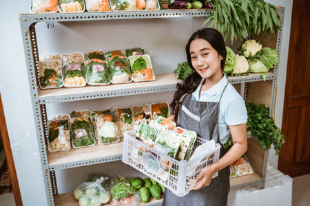 Smiling asian woman wearing apron carrying basket of fresh vegetables