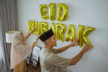 muslim couple decorating their house with eid mubarak textの写真素材