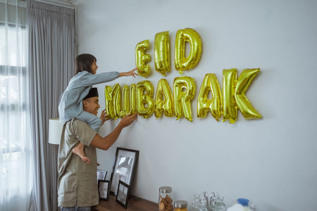 father and daughter muslim decorating eid mubarak letter made of baloon