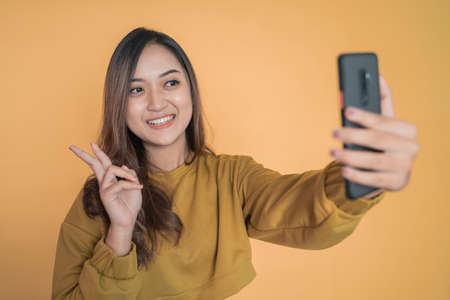 beautiful young woman selfie using phone camera with v signの写真素材