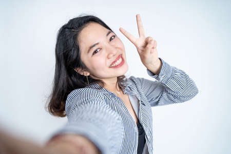 young woman selfie using mobile phone camera with v signの写真素材
