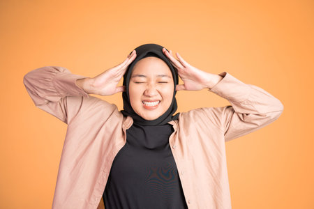 Asian woman in hijab holding head with headache