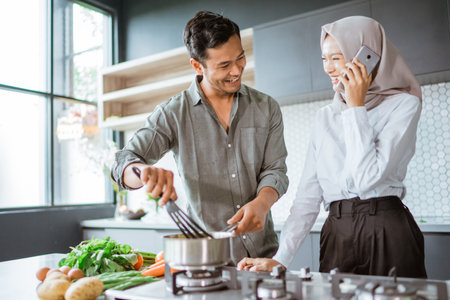 muslim couple cooking their food in the kitchen while wife taking a phone callの写真素材