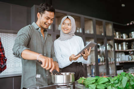 muslim couple cooking together in the kitchen while look at videoの写真素材