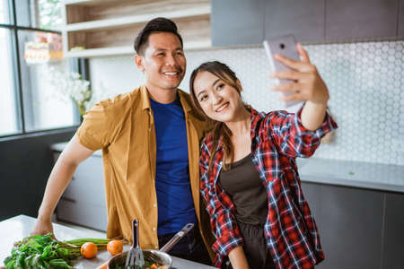 asian couple taking selfie while cooking together in the kitchenの写真素材