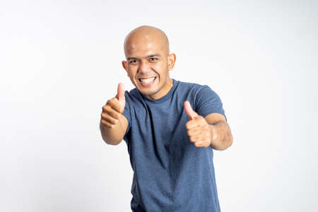 smiling asian bald man showing two thumbs up while standingの写真素材