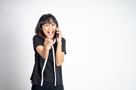 Young asian woman laughing while making a call using a cell phone on isolated backgroundの写真素材