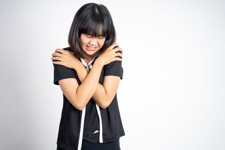 young woman feeling cold with both hands hugging her arms standing on isolated backgroundの写真素材