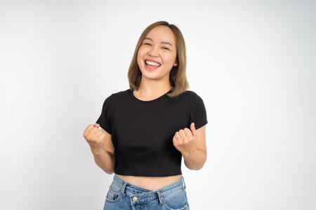 Excited asian woman clenching hands while celebrating success on isolated background