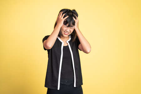 frustrated Asian young woman holding head with headache on isolated orange backgroundの写真素材