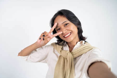 attractive woman take a selfie using mobile phone camera with v sign finger gesture on isolated backgroundの写真素材