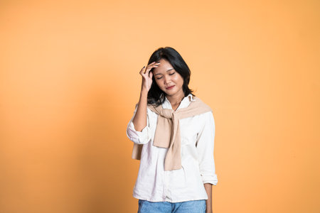 frustrated Asian young woman holding head with headache on isolated orange backgroundの写真素材