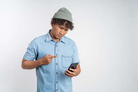 confuse young man while looking at his smartphone isolated backgroundの写真素材