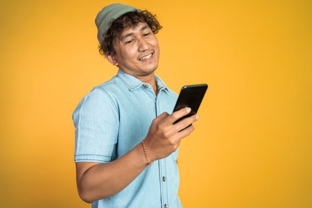 happy asian young man looking at the screen of a mobile phone on isolated background