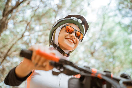 bottom view of attractive veiled girl in sunglasses smiling while riding bicycle in parkの写真素材