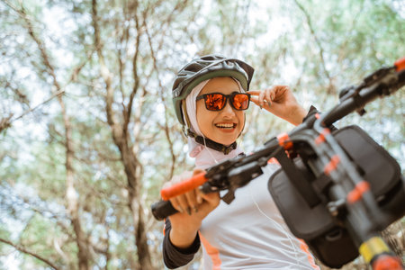 veiled asian girl holding sunglasses smiling while cycling in parkの写真素材