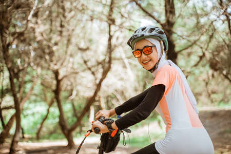 veiled girl in sunglasses smiling wearing earphones cycling in parkの写真素材