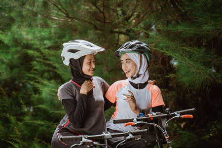 two veiled girls chatting while enjoying cycling together in the morningの写真素材