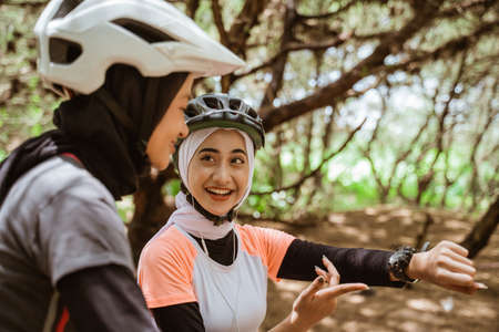 Two asian women cycling and one showing his watch during a cycling break in the parkの写真素材