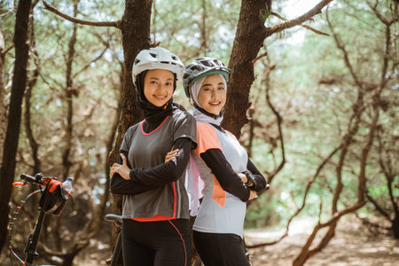 two smiling veiled women standing back to back while cycling in the park