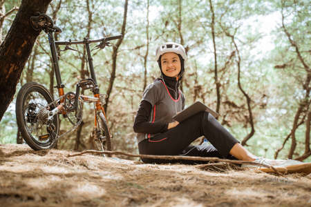 veiled girl sitting wearing earphones and using tablet while cycling in the parkの写真素材
