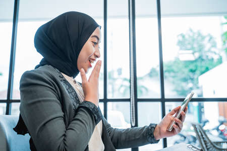 portrait of happy suprised businesswoman with hijab while looking at her phoneの写真素材