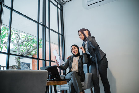 excited two muslim businesswoman raise their arm while looking at the business report